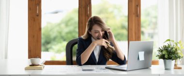Smiling asian business woman at work talking on phone and taking notes, sitting at her working place in office, copy space. banner
