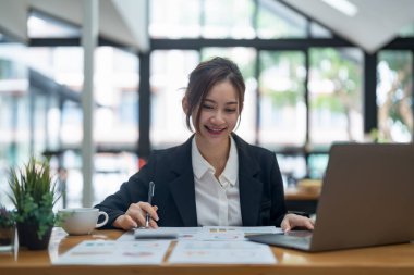 Business woman accountant calculate business report and marketing data, financial graph while working on laptop computer with spreadsheet on office desk