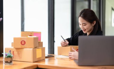 young business owner writing address on cardboard box. small business entrepreneur SME. Shipping shopping online