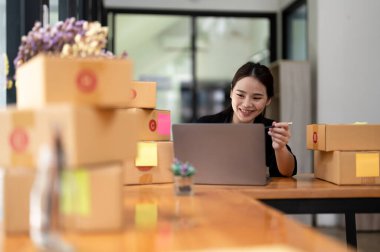 Business woman owner with parcel box for delivery and using laptop at home office. Entrepreneur small business working at home