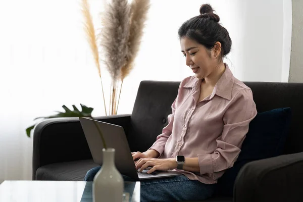 Smiling asian young woman working on laptop at home office. Young asian student using computer remote studying, virtual training, e-learning, watching online education webinar at house.