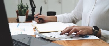 accountant working on calculator and laptop computer to calculate business data during make note at notepad, accountancy document at office.