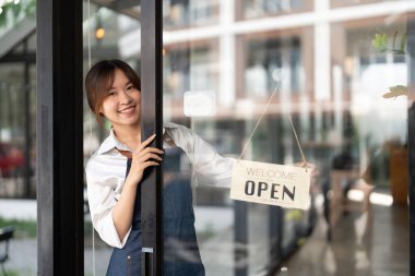 Önlüklü güzel Asyalı genç barista kadın elinde tabletle kafenin önünde açık tabela panosuyla dikiliyor. İş sahibi başlangıç konsepti.