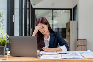 Tired and stressed young asian woman sitting at her working place