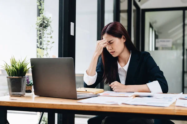 Tired and stressed young asian woman sitting at her working place