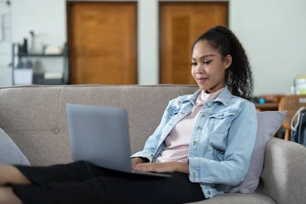 Young woman sitting on sofa at home video call chatting with friends using a laptop at home