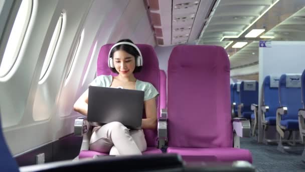 飛行機のファーストクラスで窓の近くに座ってノートパソコンを使用してアジアの若い女性 旅行やビジネスの概念 — ストック動画