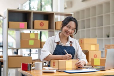 Sevkiyat çevrimiçi, sahibi iş yerindeki karton kutunun üzerine adres yazıyor. Küçük işletme girişimcisi KME ya da evde kutu ile çalışan serbest çalışan Asyalı kadın.