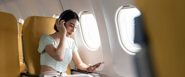 在飞机飞行过程中 带着手机和耳机听音乐的年轻女子 — 图库照片