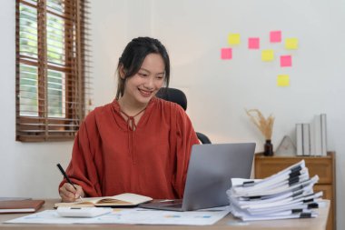 İş kadını not alıyor ve beyaz bir masada hesap makineleri ve dizüstü bilgisayarlar kullanıyor. Muhasebe kavramı.