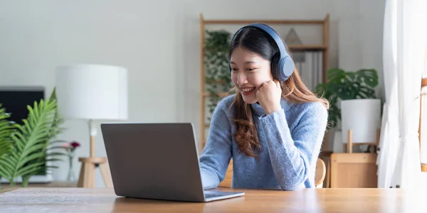 Young asian woman talk on video call at the table using headphones. Online remote work or learning concept.
