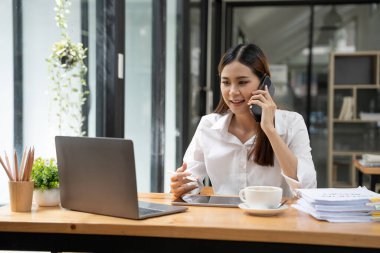Asyalı iş kadını dizüstü bilgisayar kullanıyor ve ofiste hesap makinesi ile çalışıyor, mali raporu, iş planı yatırımını, mali analiz konseptini analiz etmeyi planlıyor.