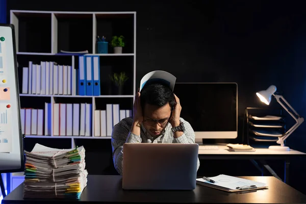 Businessman making mistake about financial business.Exhausted and tired worker surrendering to fatigue working and sleepy worker on desk with laptop on head after late night work at office