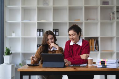 Dizüstü bilgisayar ve evraklarla birlikte çalışan iki çok ırklı profesyonel meslektaş. Kadın akıl hocası ve genç profesyonel yaratıcı ofiste oturuyor.