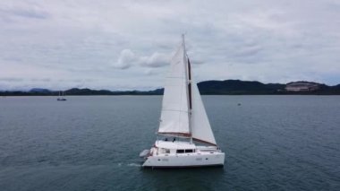 Yelkenli katamaran yelkenleri yükseliyor. Tropiklerde kıyıda yavaşça yürüyor.