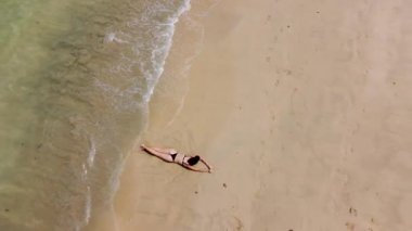 Tropikal bir plajın kıyısında bir kız yatıyor.