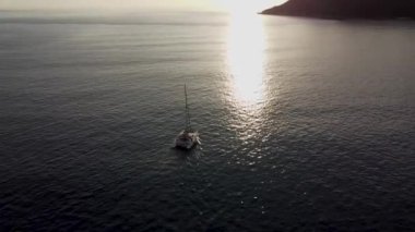 Yelkenli katamaran güneş ışınlarıyla dalgaların üzerinde yüzer gün batımını görmek için yüksekten bakar.