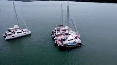 Körfezde duran yelkenli tekneleri, körfezde demirleyen büyük bir şirketin katamaranları ile yelken açmak, insansız hava aracı manzarası.