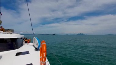 Phuket, Tayland, 20 Aralık 2019: Bir grup turist yelken altındaki bir deniz yolculuğu sırasında yelkenli bir katamaranın pruvasında yastıklar üzerinde iletişim kuruyor