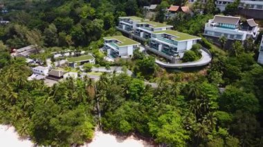 Tropik bir adanın deniz kıyısında duran özel villalar kompleksi, deniz kıyısındaki lüks konutların insansız hava aracı manzarası.