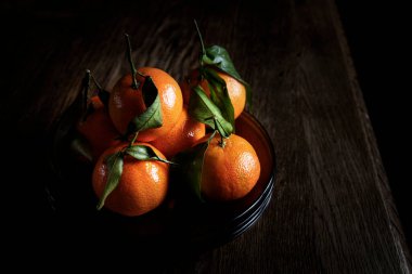 Kırsal ahşap masa ve arka planda taze mandalina tabağı.