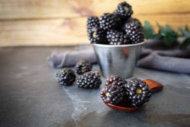 Taze ve olgun böğürtlenli tahta kaşık ve böğürtlenli metal kase. Taze meyve. Yemek fotoğrafçılığı