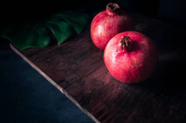 Koyu arkaplanlı, tropikal bir yaprağın üzerinde taze, güzel kırmızı narlar. İştah açıcı, olgun ve yemeye hazır. Huysuz meyve fotoğrafçılığı
