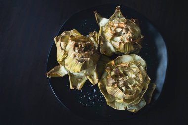 Koyu tabakta pişmiş enginar çiçekleri ve koyu ahşap arka planı.