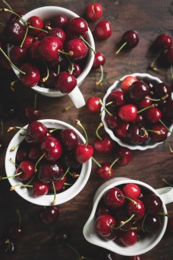 Koyu ahşap bir masada beyaz seramik bardaklarda nefis kirazlar.