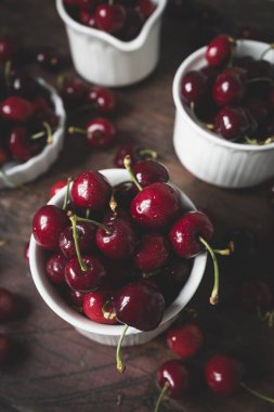 Koyu ahşap bir masada beyaz seramik bardaklarda nefis kirazlar.
