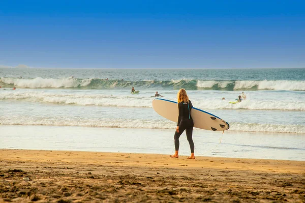 Las Canteras Plajı, Las Palmas, Grand Canary Adası. Dünyanın en büyük ikinci sörf plajı. Uzun saçlı sarışın kadınlar sörf tahtasıyla suya doğru yürüyorlar.