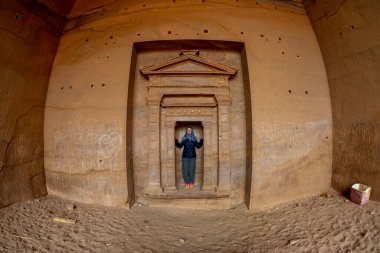 Olgun kadın, Petra Jordan 'da, tapınağın önünde mavi bir eşarp takmış ve Petra Jordan 2020 Şubat' ında kayaya oyulmuş güzel manzaranın tadını çıkarıyor.