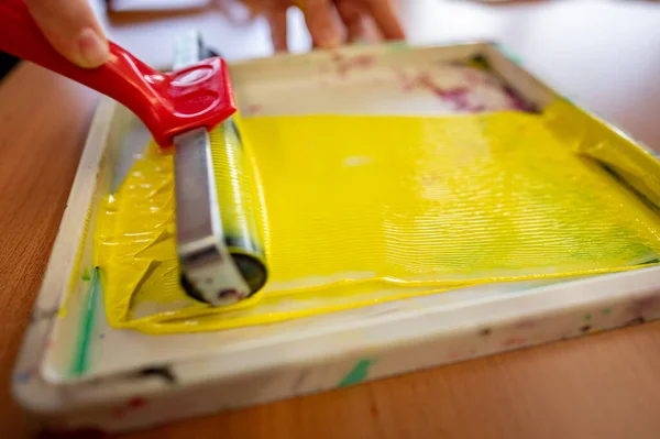 Roll of yellow paint prepared in a tray in a worker\'s hand before painting