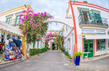 3 Şubat 2022 Puerto de Mogan Kanarya Adası İspanya Pembe kırmızı çiçekli dar sokaklarla dolu bir kasaba zemin kattaki dükkanları turistler tarafından ziyaret edilen renkli binalarla dolu.
