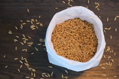 Beyaz kağıt torba ve 1 kilo yulaf ezmesi. Koyu ahşap masada tohumlar.