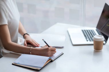 Kapatın. Evde dizüstü bilgisayarla not alan bir kadın..