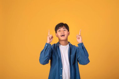 Genç bir Asyalı adamın portakal rengi arka planda parmağını göstermesi..