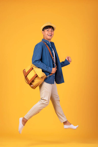 Young asian man wearing a hat and a backpack jumping up ready to go on a trip. On orange background