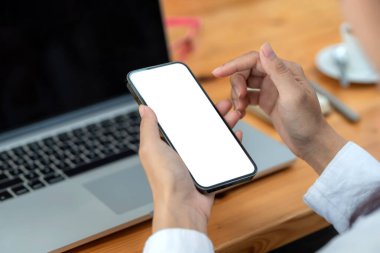 Close-up smartphone blank white screen in the hand of a businesswoman work at the office. Mock up.