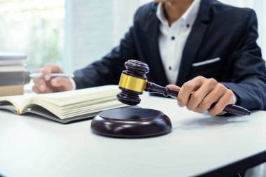Attorney holding an auction hammer and opening a book sitting in an office.