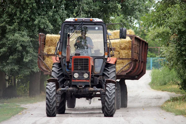 Traktör, köy yolu boyunca büyük bir karavanla saman taşıyordu.