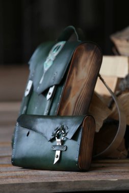 Yeşil deri cüzdanı olan sırt çantası, yakacak odununun arka planında.
