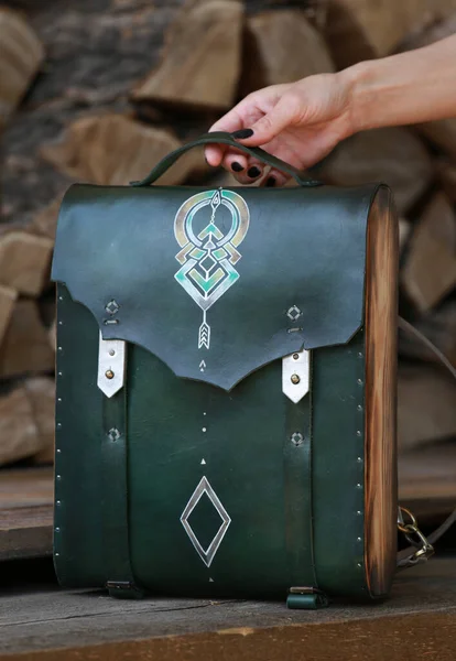 woman's hand holds a backpack bag made of green leather and wood