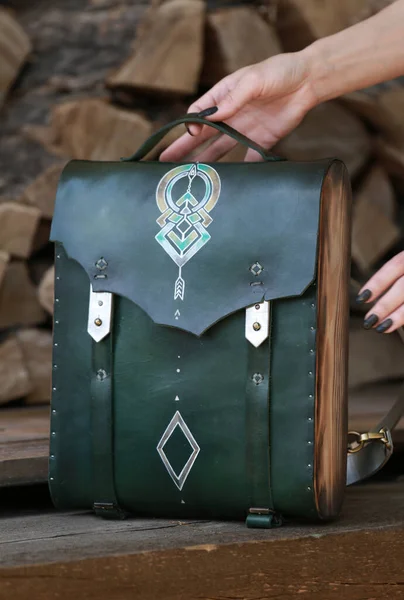 woman's hand holds a backpack bag made of green leather and wood