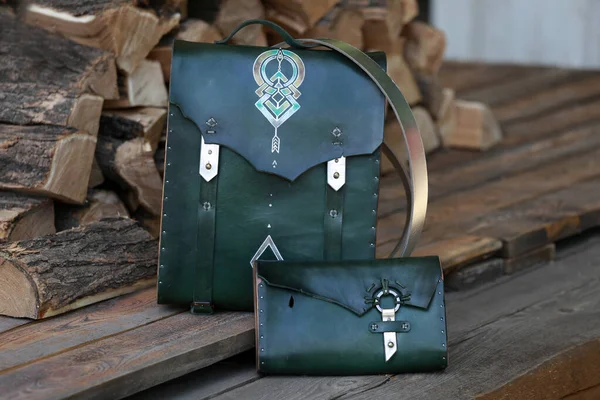 bag-backpack with a green leather wallet, against the background of firewood
