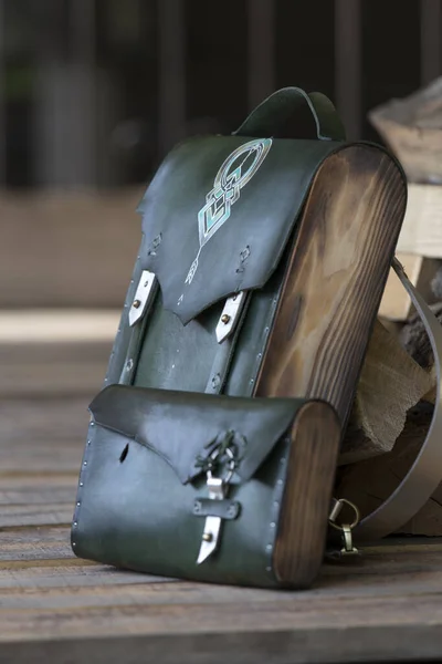 bag-backpack with a green leather wallet, against the background of firewood