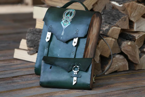bag-backpack with a green leather wallet, against the background of firewood