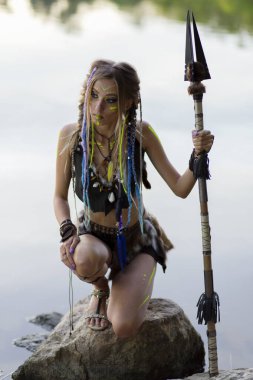 Ortaçağ kürklü, savaş boyalı, ormanda nehrin arka planında mızraklı güzel amazon kadın..
