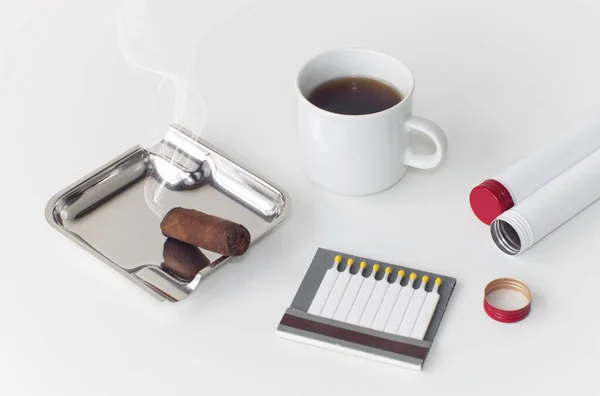 Ashtray with a smoldering cigar a cup of coffee and an open box of matches, on an isolated white background