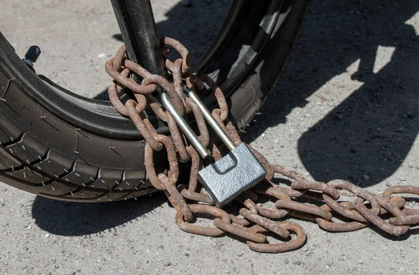 motorcycle wheel fastened with a rusty chain and lock, close-up